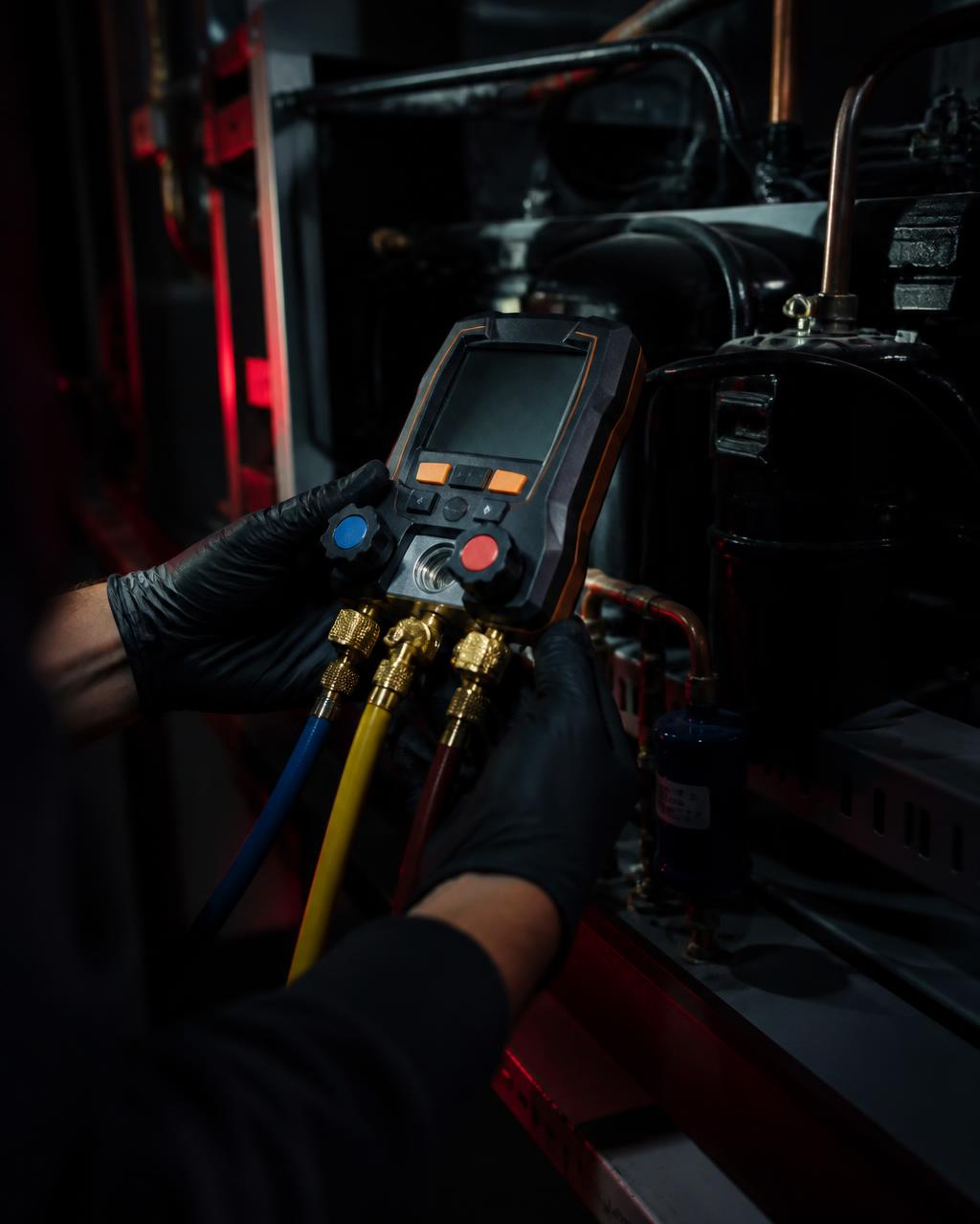 Technician taking refrigerant readings with digital manifold gauges on a refrigeration rack
